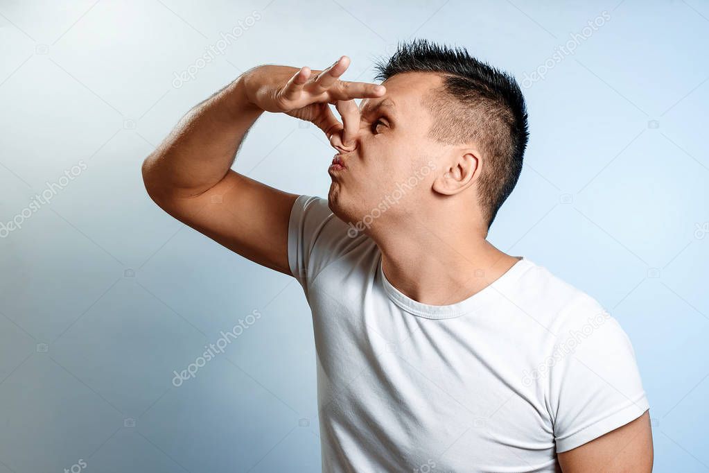 Close-up portrait of a man, closes his nose with his hands. On a light background. The concept of bad smell, stench.