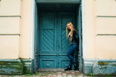 Marihuana yaprağı ağzında tutarak ve eski kapıya yaslanmış retro güneş gözlüğü takıyor şapkalı hippi sarışın kız... Yumuşak ışık, sokak stili.