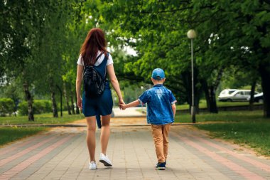Genç bir anne ve oğlu güzel yaz park boyunca yürüyor. Bir çocuk ve güzel bir kadın yürüyüş ve eğleniyor. Aile portre açık havada.