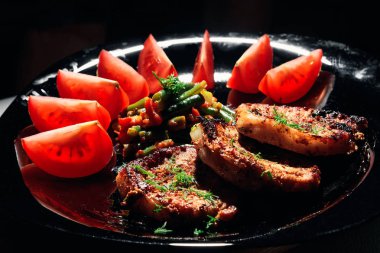 Siyah bir tabakta sebze ile domuz eti biftek