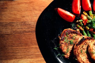 Siyah bir tabakta sebze ile domuz eti biftek