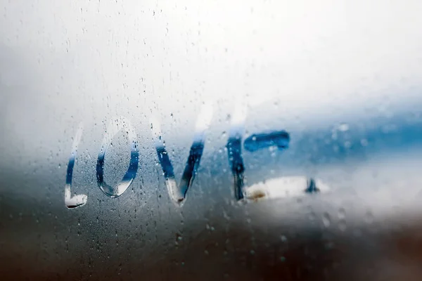 Women Hand's drawing LOVE word on glass window with water drop concept design for valentine's day or wedding background.