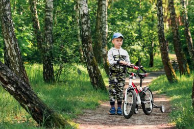 Sabahın erken saatlerinde ormanda bisiklete binen bir çocuk. Kasklı çocuk dışarıda bisiklet sürüyor.