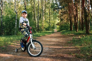 Sabahın erken saatlerinde ormanda bisiklete binen bir çocuk. Kasklı çocuk dışarıda bisiklet sürüyor.