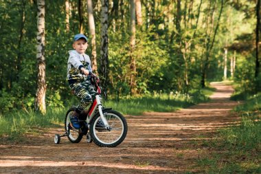 Sabahın erken saatlerinde ormanda bisiklete binen bir çocuk. Kasklı çocuk dışarıda bisiklet sürüyor.
