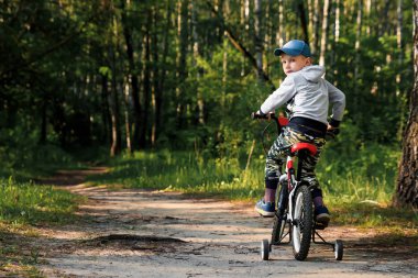Sabahın erken saatlerinde ormanda bisiklete binen bir çocuk. Kasklı çocuk dışarıda bisiklet sürüyor.