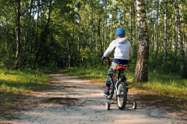 Sabahın erken saatlerinde ormanda bisiklete binen bir çocuk. Kasklı çocuk dışarıda bisiklet sürüyor.