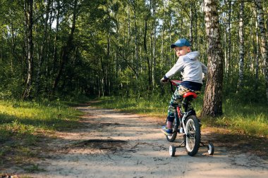 Sabahın erken saatlerinde ormanda bisiklete binen bir çocuk. Kasklı çocuk dışarıda bisiklet sürüyor.