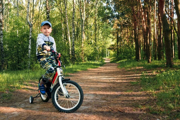 Sabahın erken saatlerinde ormanda bisiklete binen bir çocuk. Kasklı çocuk dışarıda bisiklet sürüyor.