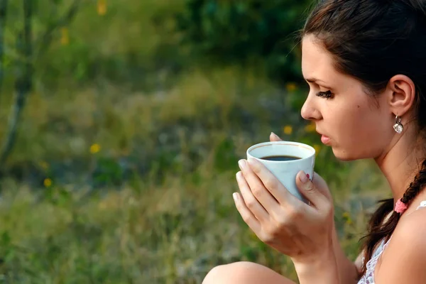 A young girl drinks coffee and looks into the distance to the sunset, waiting for someone. The concept of expectation, longing, fantasy, dreams. Copy space.