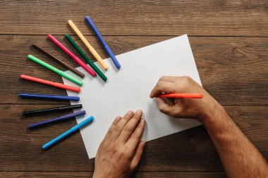 Sanatçı yakın çekim, elinde bir flamaster dağınık renkli keçe bahşiş kahverengi ahşap bir masa üzerinde yakınındaki boş kağıdın üzerinde tutar. Yukarıdan görüntüleyin. Kopya alanı.