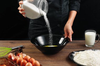 Erkek Şef şef dökülen şeker siyah mutfak eşyaları ahşap kahverengi tabloda bir plaka üzerinde eller. Şef hamur kneads. Siyah arka plan. Yemek yemek kavramı. Yakın çekim. Kopya alanı.