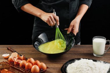 Yumurta kırbaçlanan. Şef eller yakın çekim çırpma teli bir siyah arka plan üzerine yumurta. Doğal ışık, biraz görüntü tonda. Kopya alanı.