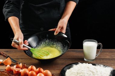 Yumurta kırbaçlanan. Şef eller yakın çekim çırpma teli bir siyah arka plan üzerine yumurta. Doğal ışık, biraz görüntü tonda. Kopya alanı.