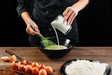 Erkek elinde Şef bir plaka üzerinde bir ahşap kahverengi masa siyah bir kase içine süt dökülen. Şef hamur kneads. Siyah arka plan. Yemek yemek kavramı. Yakın çekim. Kopya alanı.