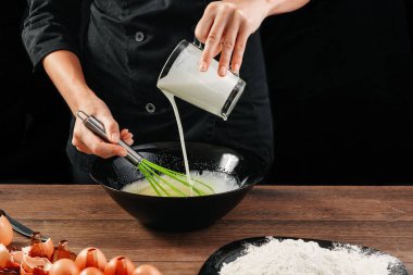 Erkek elinde Şef bir plaka üzerinde bir ahşap kahverengi masa siyah bir kase içine süt dökülen. Şef hamur kneads. Siyah arka plan. Yemek yemek kavramı. Yakın çekim. Kopya alanı.