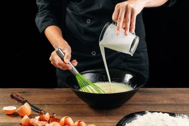 Erkek elinde Şef bir plaka üzerinde bir ahşap kahverengi masa siyah bir kase içine süt dökülen. Şef hamur kneads. Siyah arka plan. Yemek yemek kavramı. Yakın çekim. Kopya alanı.