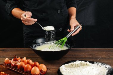 Erkek elinde Şef siyah mutfak eşyaları ahşap kahverengi tabloda un bir tabak içine dökülen. Şef hamur kneads. Siyah arka plan. Yemek yemek kavramı. Yakın çekim. Kopya alanı.