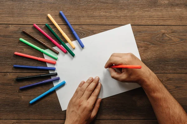 Sanatçı yakın çekim, elinde bir flamaster dağınık renkli keçe bahşiş kahverengi ahşap bir masa üzerinde yakınındaki boş kağıdın üzerinde tutar. Yukarıdan görüntüleyin. Kopya alanı.
