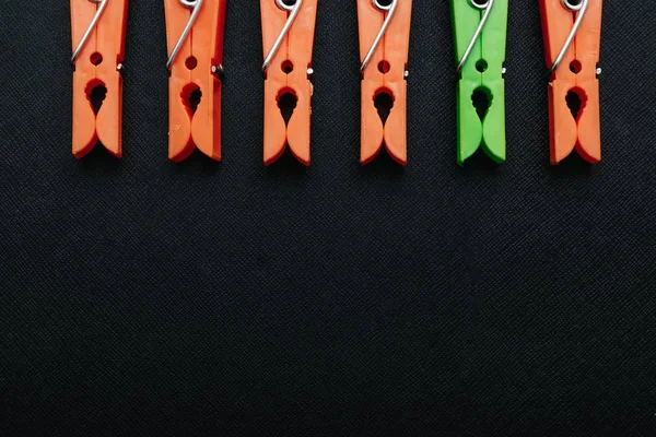 One green, linen clothespin in a row of orange, linen clothespins on a black background. Creative image, background. The concept is not like everyone else, an outcast, another.