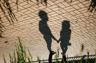 Güneşli bir günde cobblestones üzerinde şehir merkezinde el ele tutuşarak sevgi dolu bir çiftin gölgeler.