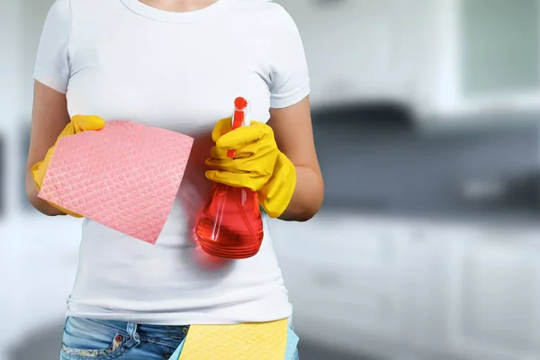 A girl, a cleaning lady with a cleanser, wearing gloves and a rag on a blurred background. The concept of cleanliness in the house, cleaning of premises, cleanliness.