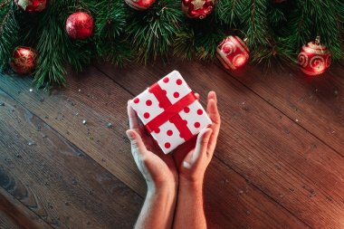 Çamın dalları ve yılbaşı süsleri ve ahşap bir masa arka plan üzerinde bir hediye vererek elleri bir çerçeve. Mutlu Noeller ve mutlu tatiller. Yukarıdan görüntülemek.