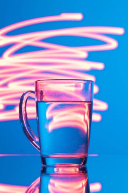 Bardak su sarı soyutlama, parlama ışık ile mavi bir arka plan üzerinde.