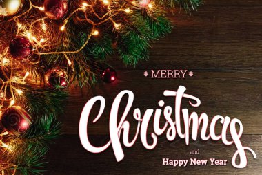Neşeli Noel ve mutlu yeni yıl yazıt, ahşap bir kahverengi masa üzerinde yeşil çam ve doğrama dalları. Noel kartı, tatil arka plan. Karışık teknik.