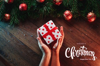 Mutlu Noeller ve mutlu yeni yıl yazıt, ahşap bir kahverengi masa üzerinde bir hediye erkek elele tutuşun. Noel kartı, tatil arka plan. Karma ortam. Yukarıdan görüntülemek.