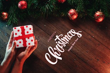Mutlu Noeller ve mutlu yeni yıl yazıt, ahşap bir kahverengi masa üzerinde bir hediye erkek elele tutuşun. Noel kartı, tatil arka plan. Karma ortam. Yukarıdan görüntülemek.