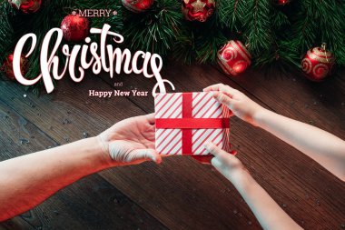 Mutlu Noeller ve mutlu yeni yıl yazıt, ahşap bir kahverengi masa üzerinde bir hediye erkek elele tutuşun. Noel kartı, tatil arka plan. Karma ortam. Yukarıdan görüntülemek.