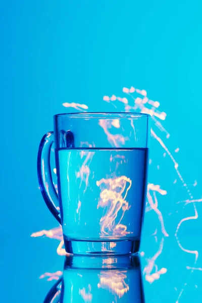 Szklanka Wody Niebieskim Tle Żółtym Abstrakcji Odblaski Światła — Zdjęcie stockowe