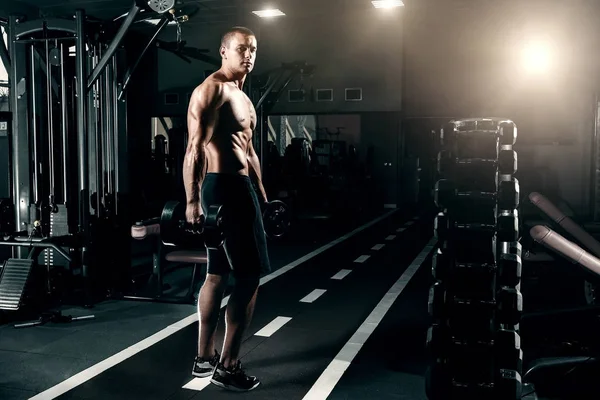 Yakışıklı olan Avrupa görünümünü vücut geliştirmeci, onun elinde dumbbells ile spor salonunda duruyor. Spor eğitim, eğitim, spor salonunda egzersiz fitness kavramı.