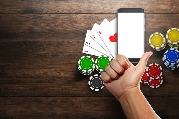 Online casino, mobile casino, top view of a mobile phone, chips cards on a wooden background. Gambling games.