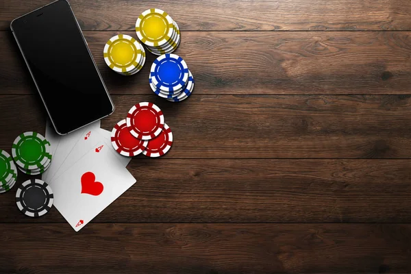 Online casino, mobile casino, top view of a mobile phone, chips cards on a wooden background. Gambling games.