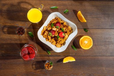 Mısır gevreği, sabah kahvaltı, Mısır gevreği, Kuru üzüm, badem, nane yaprağı, portakal suyu, çilek, en iyi görünüm, koyu ahşap arka plan, düz yatıyordu. Sağlıklı, doğru beslenme, ditox kavramı.