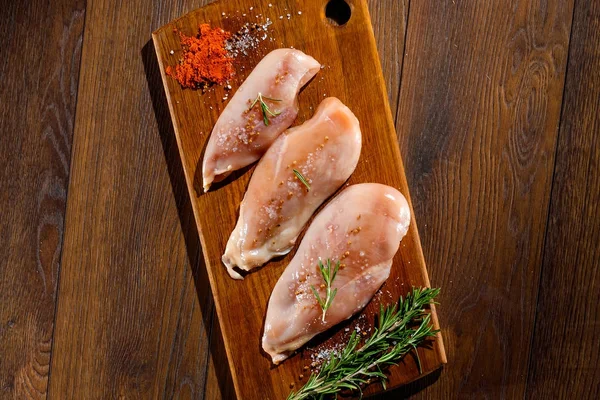 Raw, chicken fillet on a cutting board, a kitchen board, rosemary, pepper, salt, seasoning. The concept of a recipe for cooking chicken.