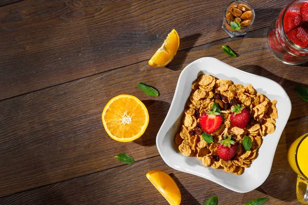 Cereal, morning breakfast, corn flakes, raisins, almonds, mint leaves, orange juice, strawberry, top view, on a dark wooden background, flat lay. The concept of healthy, proper nutrition, ditox.