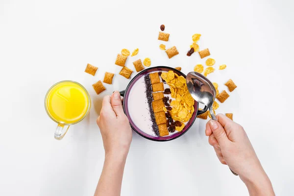 Frühstück am Morgen. Frauenhände halten einen Löffel über eine Schüssel mit hausgemachtem Joghurt und Cornflakes, Rosinen, Mandeln auf weißem Hintergrund, Draufsicht, flache Lage. Konzept der gesunden Ernährung, gesunde Ernährung, Entgiftung. co — Stockfoto