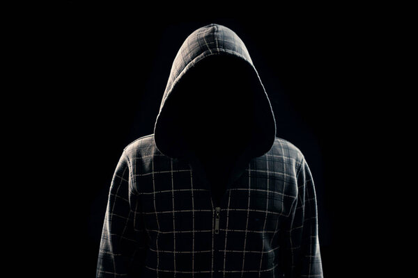 Portrait, silhouette of a man in a hood on a black background, his face is not visible. The concept of a criminal, incognito, mystery, secrecy, anonymity.