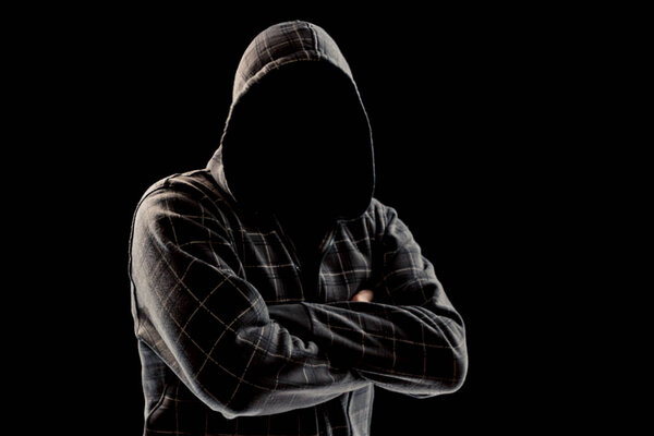 Silhouette of a man in a hood on a black background, his face is not visible, he folded his arms over his chest. The concept of a criminal, incognito, mystery, secrecy, anonymity.