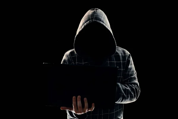 Portrait, silhouette of a man in a hood on a black background, his face is not visible. The concept of a criminal, incognito, mystery, secrecy, anonymity.