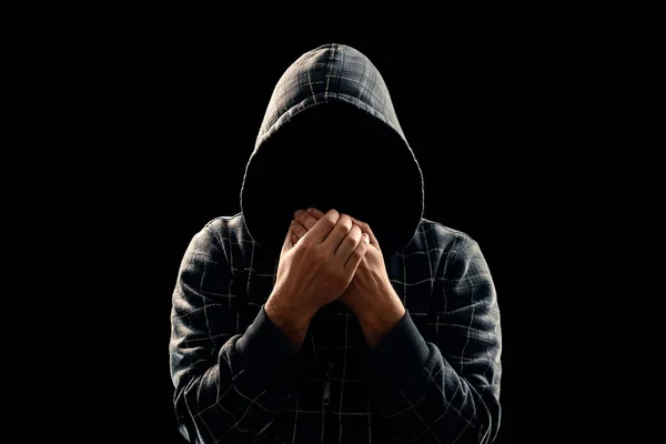 Silhouette of a man in a hood on a black background, his face is not visible, something that shows his hands. The concept of a criminal, incognito, mystery, secrecy, anonymity.