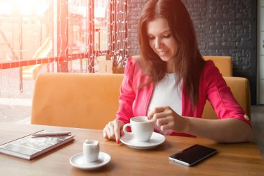 Genç bir kız şeker bir fincan kahve kıpırdanırken, ahşap bir stolikos arkasında bir kafede oturuyor. İş yemeği, modern kız.