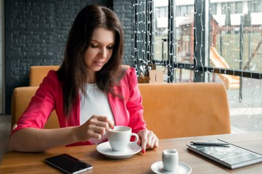 Genç bir kız şeker bir fincan kahve kıpırdanırken, ahşap bir stolikos arkasında bir kafede oturuyor. İş yemeği, modern kız.