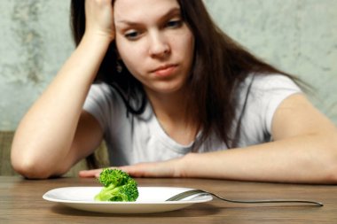 Anoreksiya Nervoza ya da küçük yeşil sebze plaka üzerinde sahip bulimia ile ilgili üzgün genç esmer kadın. Diyet sorunları, yeme bozukluğu.