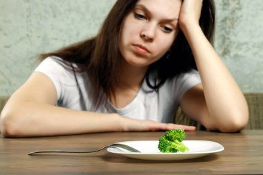Anoreksiya Nervoza ya da küçük yeşil sebze plaka üzerinde sahip bulimia ile ilgili üzgün genç esmer kadın. Diyet sorunları, yeme bozukluğu.