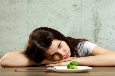 Anoreksiya Nervoza ya da küçük yeşil sebze plaka üzerinde sahip bulimia ile ilgili üzgün genç esmer kadın. Diyet sorunları, yeme bozukluğu.