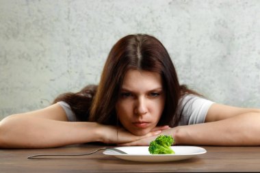 Anoreksiya Nervoza ya da küçük yeşil sebze plaka üzerinde sahip bulimia ile ilgili üzgün genç esmer kadın. Diyet sorunları, yeme bozukluğu.